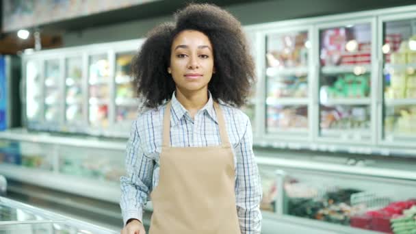 穿着围裙的女店员形象地看着杂货店超市里的相机 非裔美国黑人女工卖家或小企业主 日用品市场微笑 — 图库视频影像
