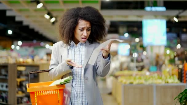 スーパーマーケットの食料品店で紙の小切手を取る女性の買い物客は 高値で非常に驚いています インフレ率の上昇 ショッピング後のチェックにショックを受けた モールに立っている消費者 — ストック動画