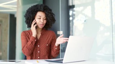 İş yerinde otururken akıllı telefondan konuşan Afro-Amerikalı genç bayan çalışanlar. Odaklanmış siyah kadın ya ortağıyla iş konuşur ya da müşterisiyle konuşur.