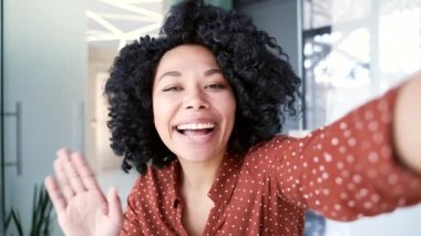 POV, gülümseyen Afro-Amerikan bir bayan çalışan iş yerinde akıllı telefon kullanarak bir video görüşmesi yapıyor. Mutlu siyah kadın kameraya bakıyor selfie çekiyor, el sallıyor, arkadaşıyla konuşuyor.