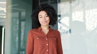 Gülümseyen genç Afro-Amerikan bayan çalışan iş yerinde kameraya bakarken başparmağını kaldırıyor. Mutlu pozitif siyahi kadın, anlaşma, başarı ve onaylama jestleri gösteriyor.