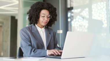 İş yerinde otururken dizüstü bilgisayarında daktilo yazan takım elbiseli Afrikalı Amerikalı genç bir iş kadını. Gözlüklü siyahi kadın bilgisayar projesinde çalışıyor, internette sohbet ediyor, e-posta yazıyor.