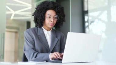Takım elbiseli mutlu Afro-Amerikan iş kadını iş yerinde otururken dizüstü bilgisayarında harika haberler okudu. Siyahi kadın zaferi kutlar, sevinir, gülümser, jest yapar evet, zafer