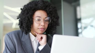 Kapatın. Ofiste dizüstü bilgisayarın başında otururken sorun çözmeyi düşünen düşünceli, konsantre, genç Afro-Amerikan iş kadını. Ciddi kadın proje veya girişim üzerinde çalışıyor