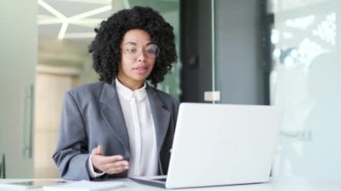 Takım elbiseli kendine güvenen Afro-Amerikan iş kadını iş yerinde dizüstü bilgisayarını kullanarak video görüşmesinde konuşuyor. Siyahi kadın internet konferansında iletişim kuruyor ya da iş ortağıyla sohbet ediyor.