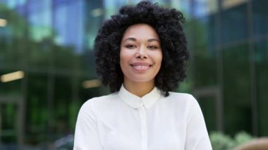 Genç ve mutlu bir Afro-Amerikan kadın çalışanın portresi bir ofis binasının yanında duruyor. Gülümseyen siyah kadın kameraya bakıyor. Başarılı bir menajerin veya ajanın vesikalığı