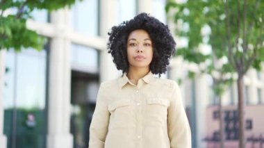 Üniversite binasının yanındaki kampüs alanında kollarını kavuşturmuş gülümseyen Afrikalı Amerikalı kız öğrencinin portresi. Caddede kameraya bakarak poz veren mutlu siyah kadın. Kafasından vur.