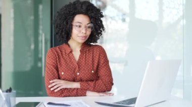Genç, mutlu bir Afro-Amerikan kadın finansçının portresi. Ofiste oturuyor. Kollarını kavuşturup kameraya bakan gülümseyen siyah kadın. Başarılı bir menajerin veya muhasebecinin vesikalığı