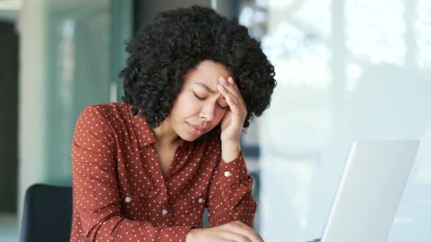疲惫不堪的年轻非洲裔美国女雇员头疼不已 只能坐在办公室的笔记本电脑上工作 不安的黑人妇女感到疼痛 用手按摩她的太阳穴和额头 — 图库视频影像
