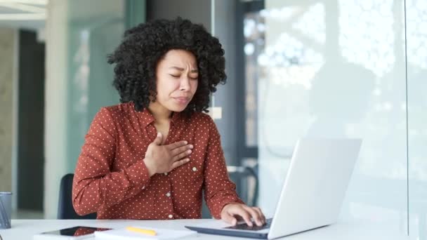胸の張力に苦しむ若いアフリカ系アメリカ人女性従業員 ビジネスオフィスの職場でデスクに座っているラップトップに取り組む心臓発作 黒人女性は緊急の医療を必要とします — ストック動画