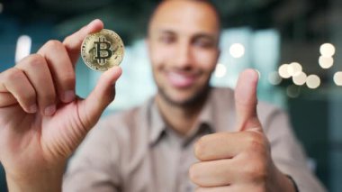 Elinde bitcoin kripto para tutan gülümseyen işadamı modern ofis merkezindeki kameraya baş parmağını kaldırmış ve kameraya tek başına bakan başarılı mutlu kripto simsarı.