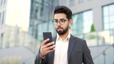 Gülümseyen yakışıklı sakallı iş adamı, ofis binasının yakınındaki caddede duran akıllı telefondan harika haberler okuduktan sonra başarıyı kutluyor. Mutlu erkek, zaferle el ele tutuşup, evet diyor. Kapat.