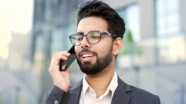 Resmi takım elbiseli, gülümseyen sakallı iş adamı ofis binasının yanındaki sokakta akıllı telefondan konuşuyor. Girişimci bir müşteriyle iletişim kurar ya da bir iş ortağıyla iletişim kurar.
