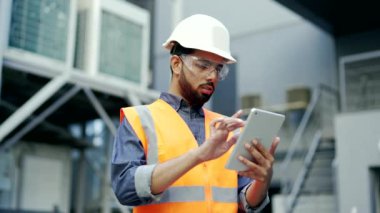 Fabrikada güvenlik kaskı ve yelek giyen profesyonel mühendis dijital tablet üzerinde çalışıyor. Ciddi endüstri müdürü. Üniforma uzmanı. Üretimi kontrol ediyor.