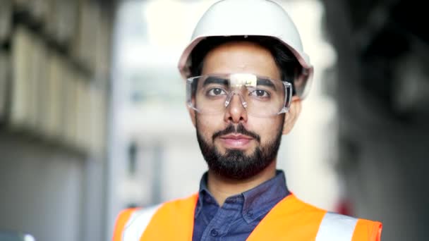 面带微笑 戴着安全帽 戴着防护眼镜 身穿背心站在工厂里的工程师的近照 穿着制服 自信的行业经理看着镜头的头像 — 图库视频影像