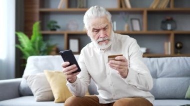 Hüsrana uğramış yaşlı bir adam, evde oturan akıllı telefondan kredi kartı numarasını girerken dolandırıcılığı keşfetti. Üzgün yetişkin erkek ellerini açar ve kameraya bakar. O bir aldatma kurbanı oldu.