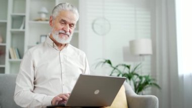 Dizüstü bilgisayarda çalışan yaşlı bir adam evdeki oturma odasında kanepede oturuyor. Olgun iş adamı mesajlaşması bilgisayardan mesajlaşma internette gezinme, online alışveriş, sohbet, uygulama bankacılığı