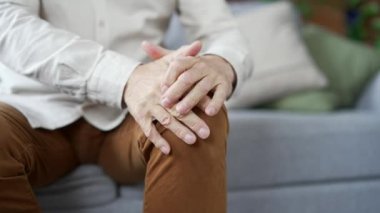 Olgun erkek eller, evdeki oturma odasında koltukta oturan diz kaslarına masaj yapıyor. Yaşlı adam diz eklem ağrısı, yürüyemiyor, hastalık krampları ve romatizmadan muzdarip.