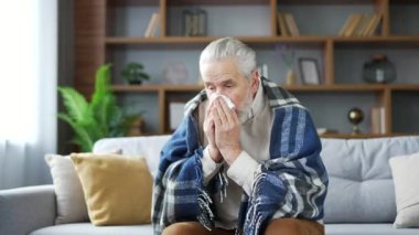 Hasta, yaşlı ve battaniyeye sarılı yaşlı bir adam, evdeki oturma odasında kanepede otururken burnunun akmasından muzdarip. Üzgün, olgun bir erkek burnunu mendille siler. Nezle, virüs ya da grip olmuş.