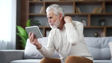 Yaşlı, yaşlı, kır saçlı bir adam evdeki oturma odasındaki koltukta dijital tablet kullanan bir doktorla video görüşmesi yapıyor. Hasta, olgun bir erkek sorunlarını anlatıyor, hastalıktan şikayet ediyor.