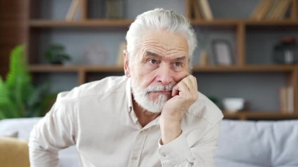 高齢の灰色の毛髪の男性は 自宅のリビングルームでソファーに座って孤独 うつ病を感じています ウプセット成熟した祖父は自分の問題について考えています 彼は不幸で失望している クローズアップ — ストック動画