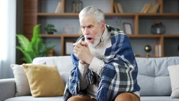 高齢の灰色の毛髪の男は 自宅のリビングルームでソファーの上に座っている毛布で覆われています Upset 成熟した 引退した 年金受給者の祖父は低温による不快感を感じる — ストック動画