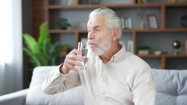 Oudere Grijze Bebaarde Man Drinkt Water Uit Een Glas Bank — Stockvideo