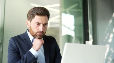 Resmi takım elbiseli ciddi düşünceli bir işadamı iş yerindeki bir laptopta çalışıyor. Yönetici bir sorunu çözmeyi düşünüyor, bilgisayardaki başlangıç projesiyle meşgul. Kapat.
