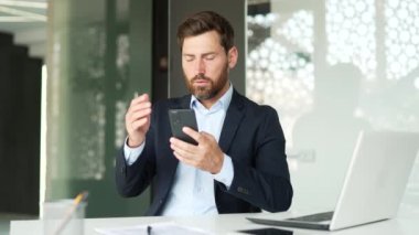 Resmi takım elbiseli sinirli işadamı iş yerinde otururken akıllı telefondan kötü haberler okuyor. Hüsrana uğramış girişimci, telefondaki olumsuz bilgiyi eleştirmekten rahatsız