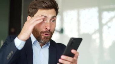 Resmi takım elbiseli mutlu iş adamı iş yerinde otururken akıllı telefondan harika haberler aldı. Neşeli bir girişimci telefonda hoş bir mesaj okur, başarıyı kutlar. Kapat.