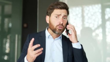 Resmi takım elbiseli kızgın işadamı iş yerindeki bir akıllı telefonla konuşuyor. Heyecanlı erkek patron, bir astıyla sorunlar hakkında duygusal olarak konuşur. Kapat.