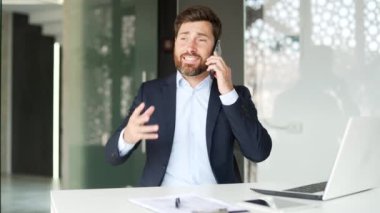 Resmi takım elbiseli kızgın işadamı iş yerinde otururken akıllı telefon kullanarak tartışıyor. Heyecanlı erkek patron, bir astıyla sorunlar hakkında duygusal olarak konuşur.