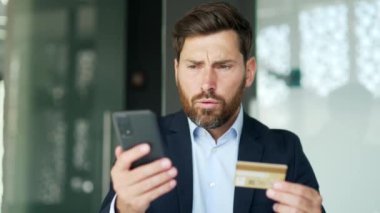 Şok olmuş işadamı iş yerindeki akıllı telefondan kredi kartını kontrol ediyor. Hüsrana uğramış üzgün bir erkek dolandırıcılıkla karşı karşıya. Hesabından para çalınmış. O bir aldatma kurbanı oldu. Kapat.