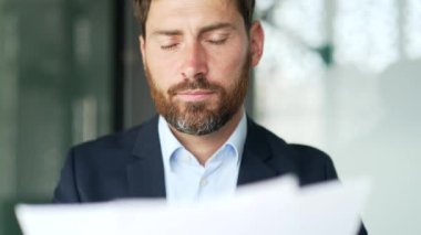 Ciddi düşünceli bir işadamı elinde belgelerle iş yerindeki bir iş yerindeki rapora bakıyor. Finansör, mali açıklamanın sonuçlarından memnun. Kapat.