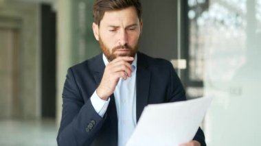 Takım elbiseli ciddi düşünceli bir işadamı iş yerinde evrak işleriyle uğraşıyor. Yönetici bir sorunu çözmeyi düşünüyor, başlangıç projesiyle meşgul. Yatırımcı verileri analiz eder. Kapat.