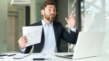 Resmi takım elbiseli kızgın işadamı ofisteki bir iş yerinde dizüstü bilgisayarla video görüşmesi yapıyor. Tatminsiz yönetici bir diyagram gösterir ve astlarına şirketin sorunlarını anlatır