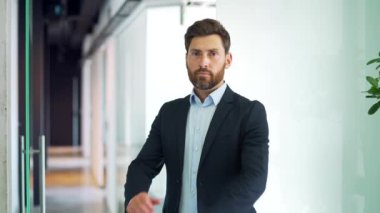 Modern ticaret ofisinde kollarını kavuşturmuş duran resmi takım elbiseli başarılı bir iş adamının portresi. İçerideki kameraya bakarak poz veren kendine güvenen sakallı girişimci. Öğretmenin kafasından.