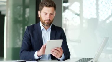 Resmi takım elbiseli iş adamı iş yerinde otururken dijital tablet kullanıyor. İşçi iletiyi okur veya yazar, bir istemci, bankacılık, e-posta kontrolü veya çevrimiçi tarama ile sohbet eder