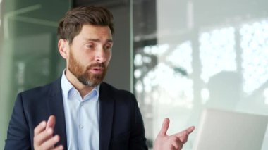 Resmi takım elbiseli kendine güvenen bir işadamı, iş yerinde oturan bir dizüstü bilgisayarla video görüşmesinde konuşuyor. Girişimcinin bir iş toplantısı var, online bir konferansta uzaktan konuşuyor. Kapat.