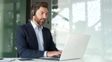 Müşteri desteğinde çalışan bir şirket operatörü bir dizüstü bilgisayarla bir video görüşmesinde konuşuyor. Kablosuz kulaklıklı merkez ajanını ara. Ofisteki şikayetleri için müşterilere yardım et. Çevrimiçi danışma