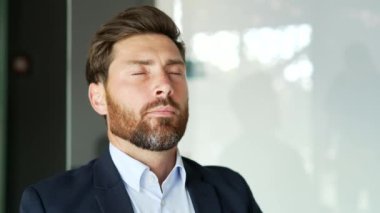 Resmi takım elbiseli, yakışıklı sakallı iş adamını yakından çek. İş yerinde gözleri kapalı dinleniyor. Sakin, mutlu ve derin nefes alan bir erkeğin portresi. Pozitif işçi işe ara verdi.