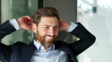 Mutlu iş adamı, iş yerindeki iş yerinde ellerini başının arkasına koyarak rahatlar. Gülümseyen işçi görevinden memnun, tatilde dinleniyor veya projeyi bitirdikten sonra kapatıyor.