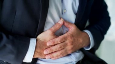 Kapatın. Erkek el, karın masajı yapıyor. Resmi takım elbiseli bir işadamı iş yerinde otururken mide ağrısı hisseder. Hasta adam mide ekşimesinden, mide iltihabından ya da spazmlardan muzdarip.