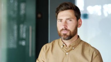 Modern iş ofisindeki iş yerinde duran gömlekli yakışıklı bir müdürün portresi. Kendine güvenen sakallı işçi kameraya içeride bakıyor. Düşünceli bir öğretmenin kafa resmi. Kapat.