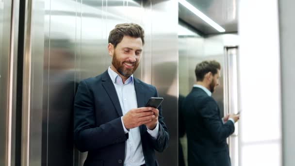 身着正装的商人站在一座现代化办公楼的电梯里 一边用智能手机 员工阅读或键入消息 浏览社交网络 查看邮件或在网上浏览 — 图库视频影像