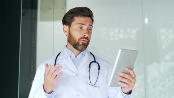 自信的医生在医院诊所用平板电脑进行视频通话 男性医务工作者医生在办公室的会议上进行远程沟通 或与病人进行在线咨询 — 图库视频影像