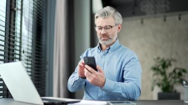 Olgun, gri sakallı iş adamı iş yerindeki akıllı telefonuna göz atıyor. Kıdemli girişimci, yazılım uygulaması kullanarak masaj, sohbet, telefon uygulamalarında bankacılık yazar.