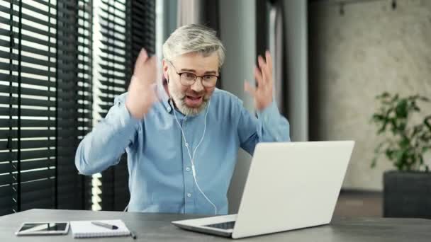 怒っている不満の成熟した灰色のひげ付きビジネスマンは ビジネスオフィスの職場に座っているラップトップを使用してビデオ通話で主張しました 興奮した上司は感情的に問題について部下と話します — ストック動画