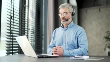 İş yerindeki bir videoda konuşan, kulaklıklı, olgun, gri sakallı bir iş adamı. Girişimcinin bir iş toplantısı var. Koç çevrimiçi kursta ya da webinar dersinde uzaktan konuşuyor.