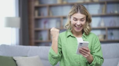 Mutlu olgun bir kadın evdeki kanepede oturan akıllı telefonlara bakarak iyi haberler alıyor. Gülümseyen kadın, internet üzerinden harika fiyat alışverişiyle tebligat aldı.
